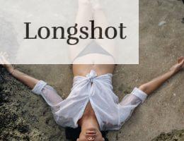 From above of full length slim female with closed eyes in white shirt and black bikini lying on sandy shore in water while enjoying time