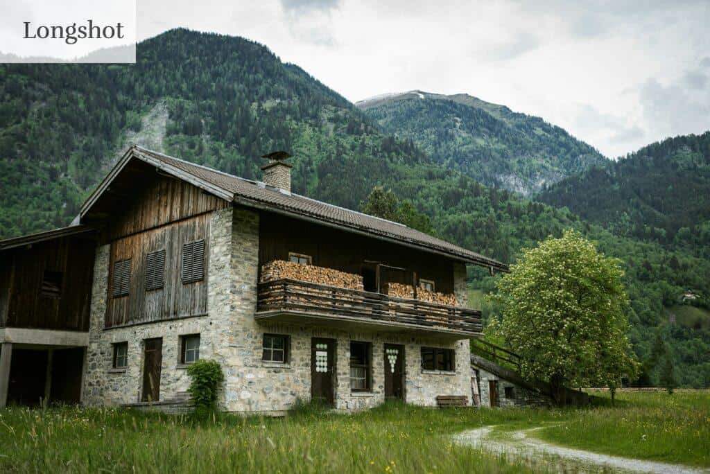 brown wooden house on green grass field near green mountain during daytime