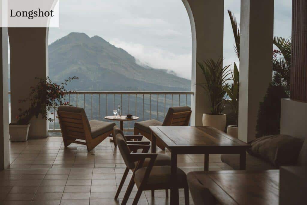 a patio with chairs and tables and a body of water in the background
