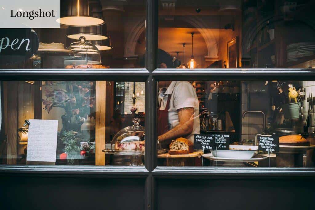Warm bakery scene in London through window showcasing pastries and chef at work.