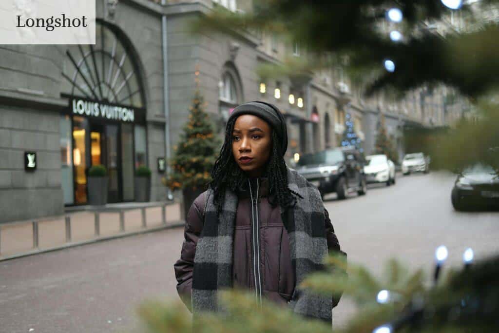 A fashionable woman in winter attire standing on a city street, near a luxury store.