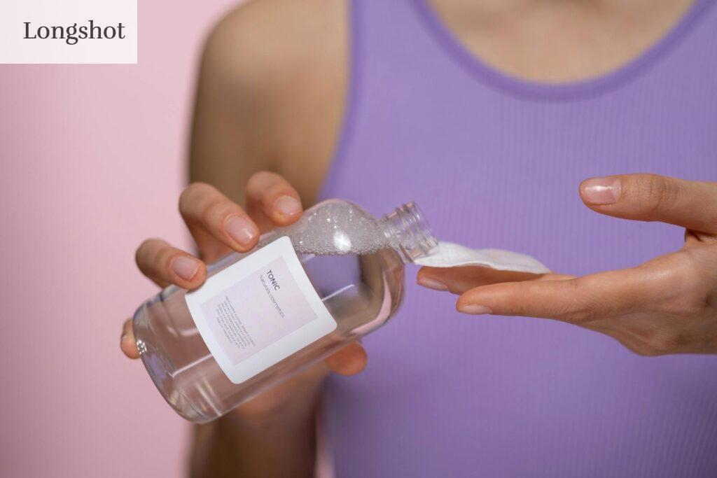 Woman applying skincare tonic with a cotton pad. Focus on hands and product in a studio setting.